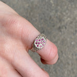A silver ring with a cluster of small pink gemstones, worn on a person's finger against a gray concrete background.