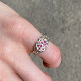 A silver ring with a cluster of small pink gemstones, worn on a person's finger against a gray concrete background.